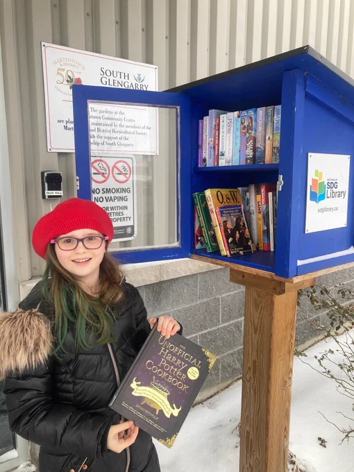 A little girl adding a book to an outdoor Little Free Library