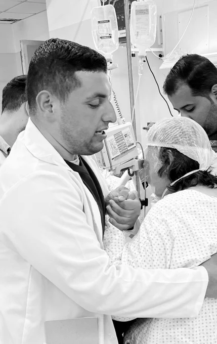 A photograph of Saleh a physiotherapist supporting a patient to mobilise in a hospital bed.
The image is in black and white