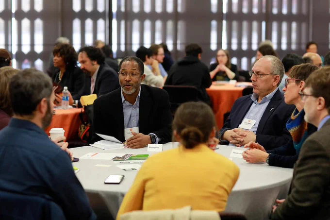 A group of adults in business clothing talk around a table.