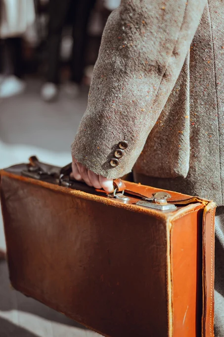 A person wearing a coat holds a brown briefcase. Photo by Clem Onojeghuo.