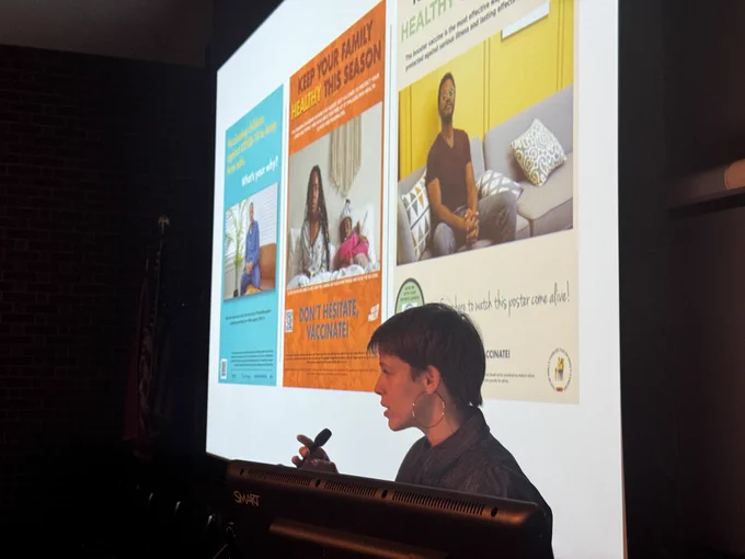 Image of a person standing in silhouette in front of a projection screen with colorful advertisements