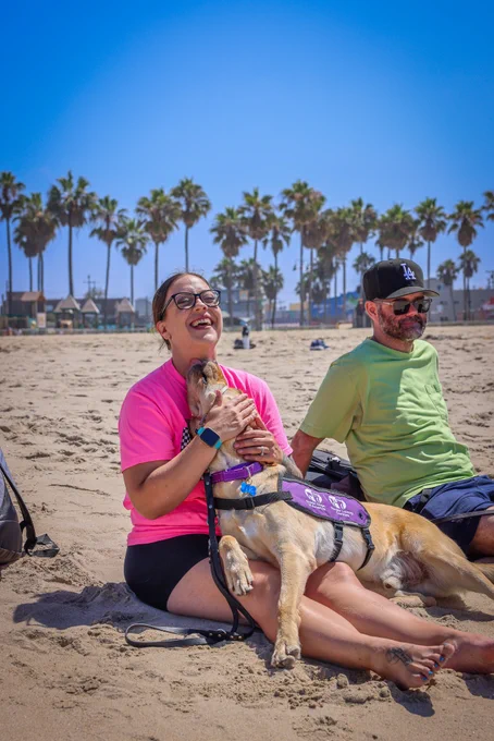 In this photo, a woman sits on the beach with her yellow Lab service dog.