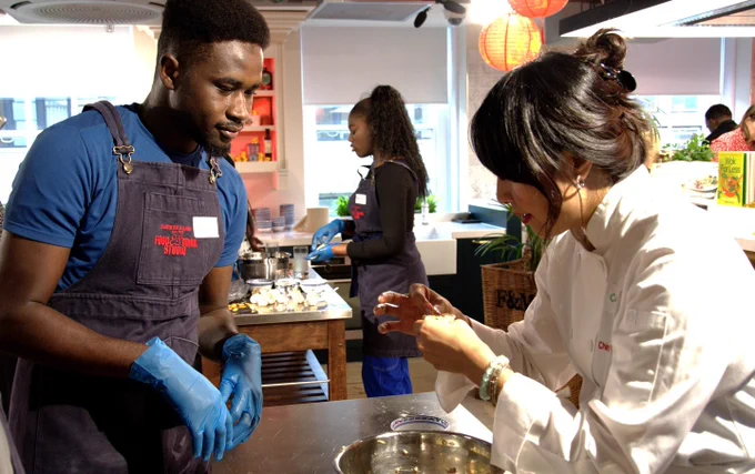 A young man looks on as a chef shows him how to prepare dumplings.
