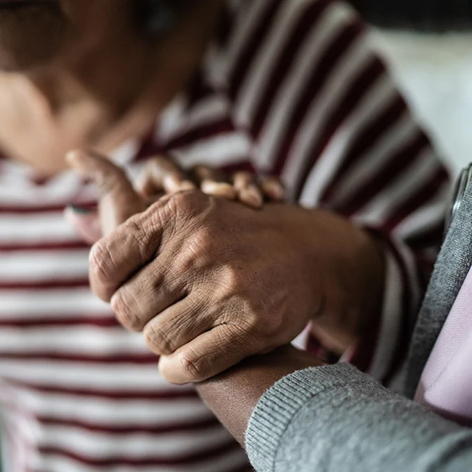 This image depicts a close-up of an older person's hand being held by a younger person's hand.