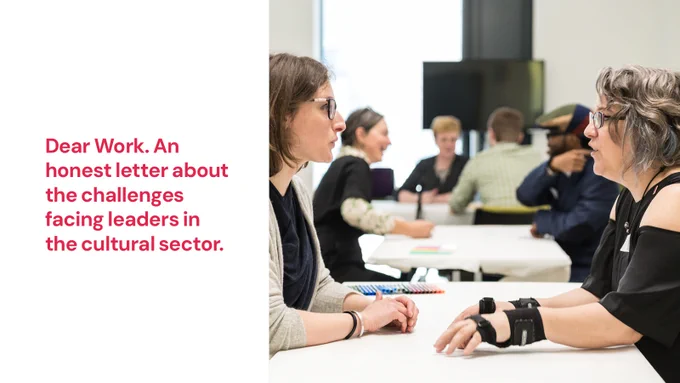 Our director Jo Verrent sits at a table across from another person. They're in conversation with their hands resting on the table. Pink text on a white background reads: Dear Work. An honest letter about the challenges facing leaders in the cultural sector.