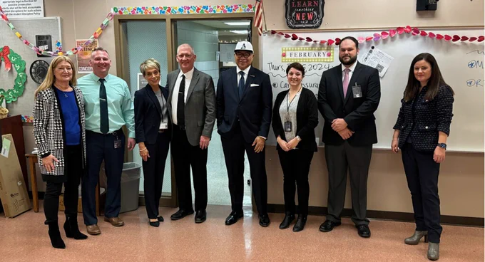 Eight people standing in a line at the front of a classroom.