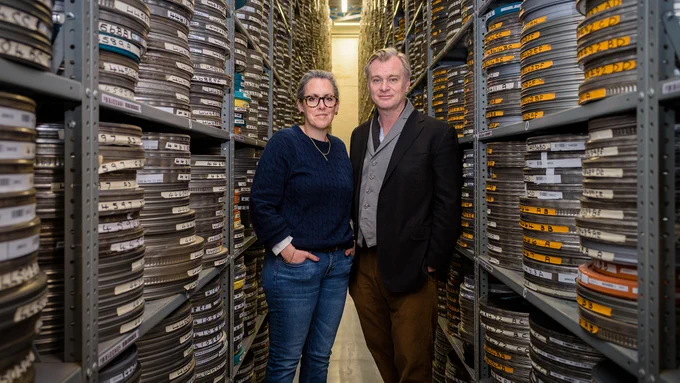 Two people posing for a photo in between high shelving holding film reels.