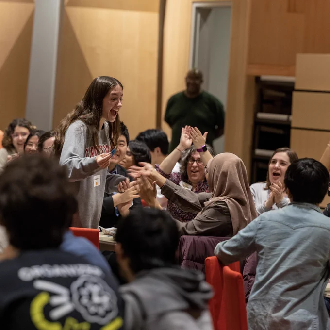 In a large group of people, a young woman who won a raffle stands up excitedly.