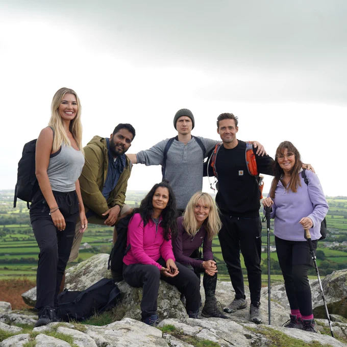 Left to right: Christine McGuinness, Eshaan Akbar, Sonali Shah, Tom Rosenthal, Michaela Strachan, Spencer Matthews and Amanda Lovett stand on the top of a hill with green fields visible behind them