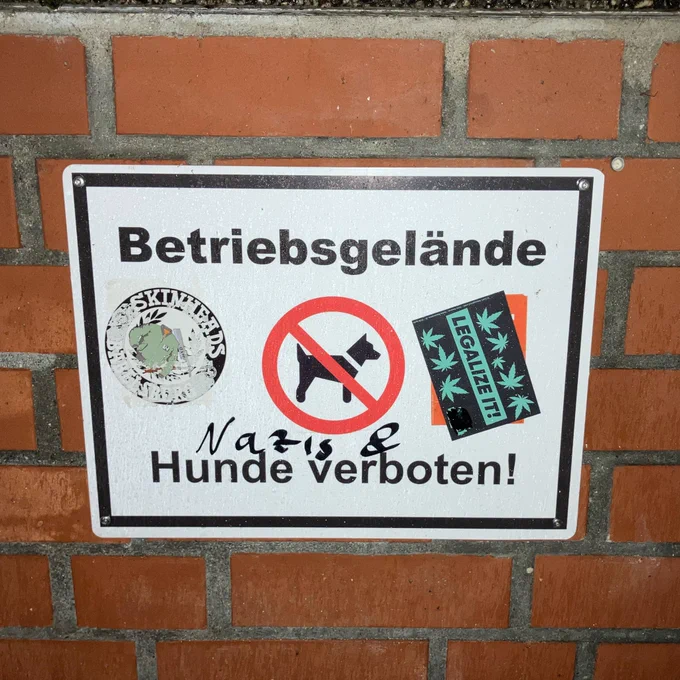 an einer roten backsteinmauer hängt ein schild auf dem steht: betriebsgelände hunde verboten. jemand hat nazis & hunde verboten daraus gemacht. 

dazu klebt noch ein sticker der red&anarchist skinheads babelsberg sowie ein legalize it - sticker.