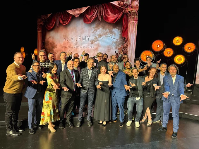 Insomniacs, PlayStation, and Marvel Games employees gathered on the DICE stage posing for a group photo. They are doing the iconic Spidey web hand gesture. 