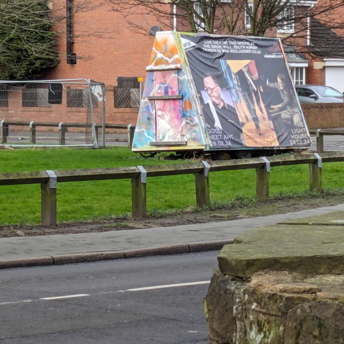 A giant banner on wooden frame on a village football pitch advertises three plays. 