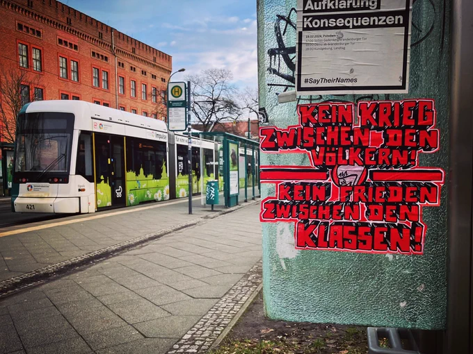 an einer kaputten glasscheibe einer telefonzelle klebt ein großes handgemaltes pasteup, es steht groß in rot: KEIN KRIEG ZWISCHEN DEN VÖLKERN! - KEIN FRIEDEN ZWISCHEN DEN KLASSEN! 

161