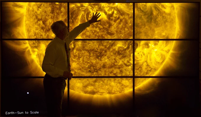 Individual standing with arm outstretched over a high-resolution nine-screen display of the sun's surface and solar activity 