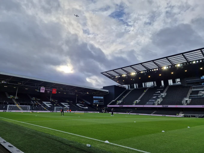 Pitch level image of the pristine Craven Cottage pitch as the clouds fill the sky and a sole plane passes over the stadium