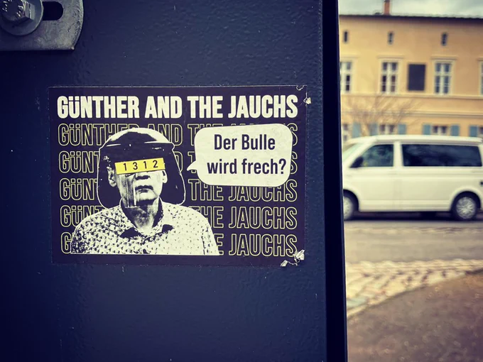 sticker auf der rückseite eines hundkotbeutelspenders: es ist ein bild von günther jauch mit polizeihelm, seine augen sind mit einem schild auf dem 1312 steht verdeckt, in einer sprechblase steht: Der Bulle wird frech?

oben und hinter dem bild steht groß: GÜNTHER AND THE JAUCHS 

https://gatj.bandcamp.com/album/menschheit-meh