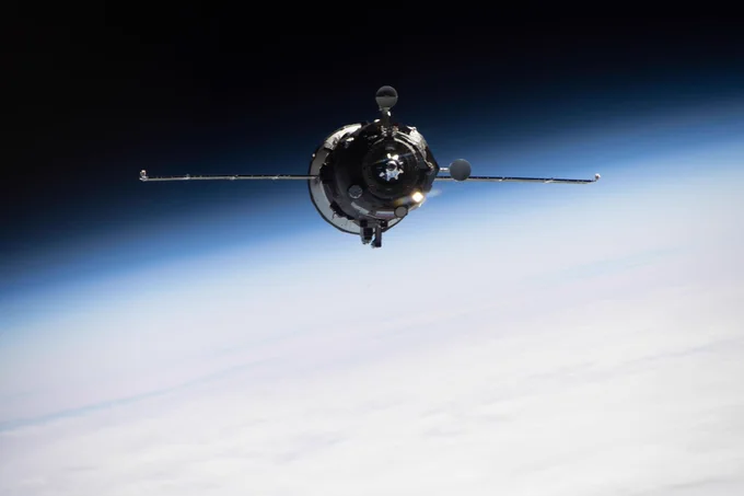A Progress cargo spacecraft in low Earth orbit approaching the International Space Station ahead of docking. The docking unit is visible and solar panels extend horizontally from the sides of the spacecraft. Earth's limb can be seen below.