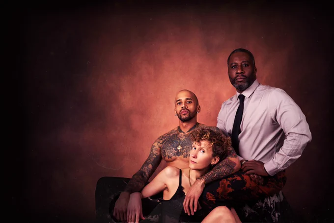 A white woman leaning against a Black male. Behind her is a mixed race male, signifying her son and the story of Oedipus.