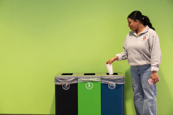 A student placing a paper cup in the recycling bin