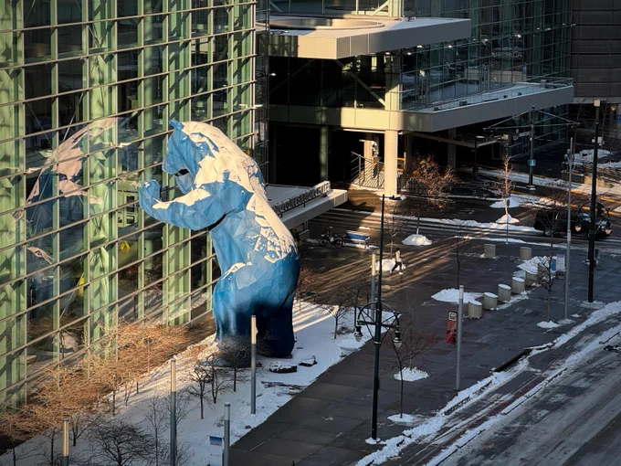 A photo of the large blue bear statue looking into the conference center, blanketed in snow.