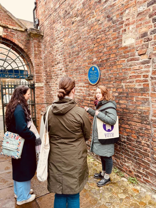 A Uncomfortable York tour guide stands in a brick alley in front of Anne Lister's blue plague.