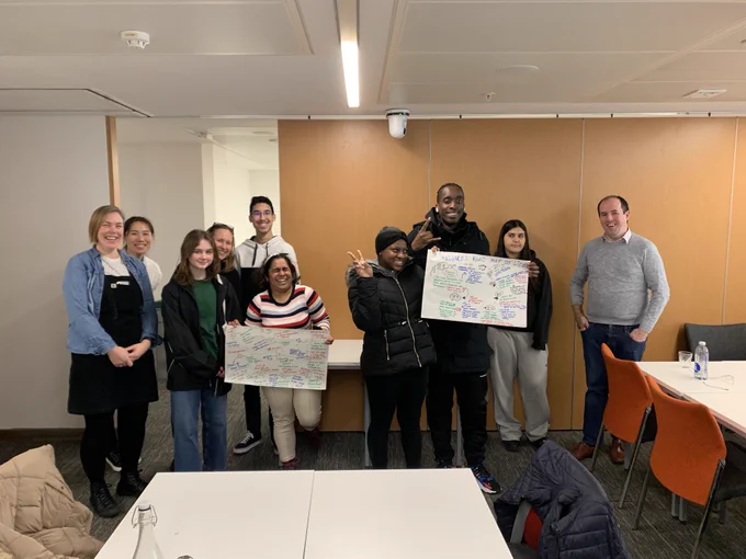 Photograph of a group of 10 people attending a workshop, holding up pieces of paper with annotations.