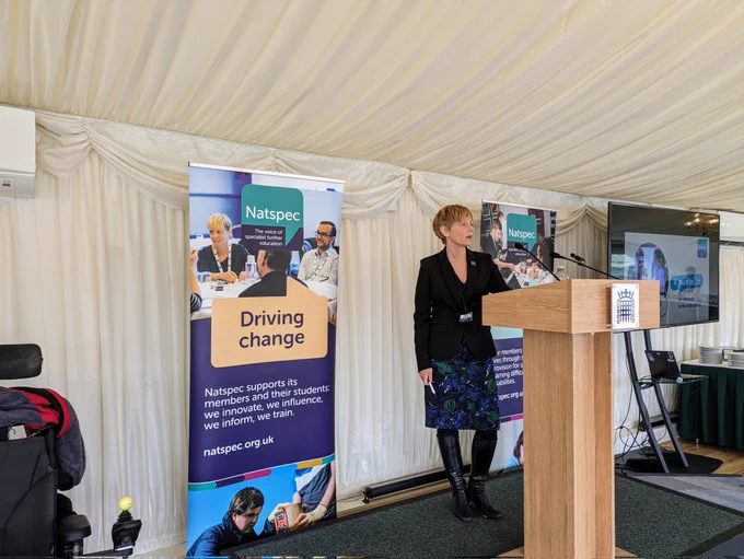 Clare Howard standing behind a lectern with Natspec banners behind her