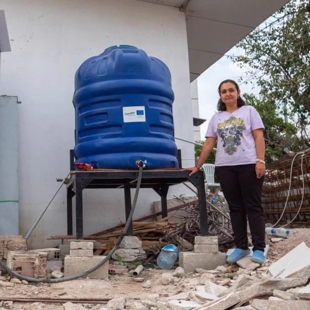 Erva stands next to the water tank delivered by Concern with EU humanitarian funding.