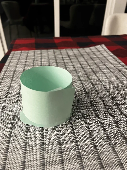 A paper “mug” made out of green paper by a 6 year old set on a gray placemat for  a “morning tea party”