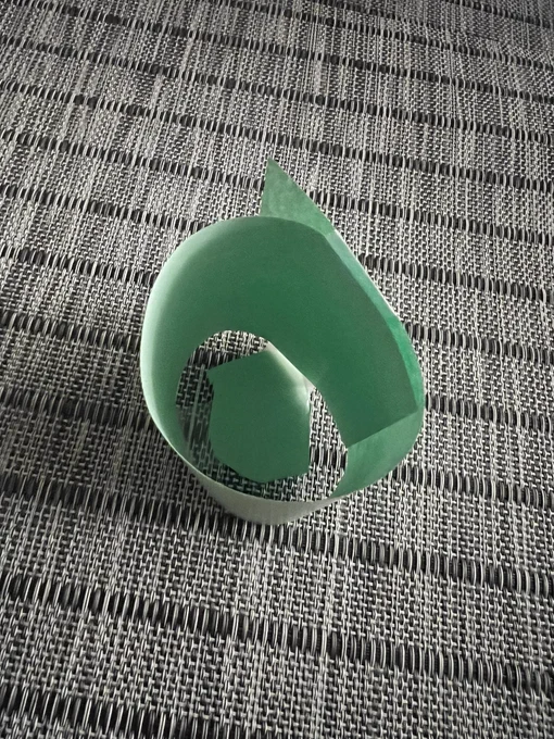 A paper “mug” made out of green paper by a 6 year old set on a gray placemat for  a “morning tea party”