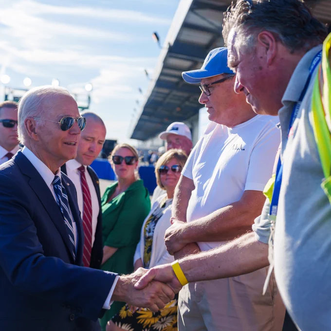 President Joe Biden wearing aviators and a black suit shakes hands with attendees after his speech announcing funding for regional clean energy hubs.