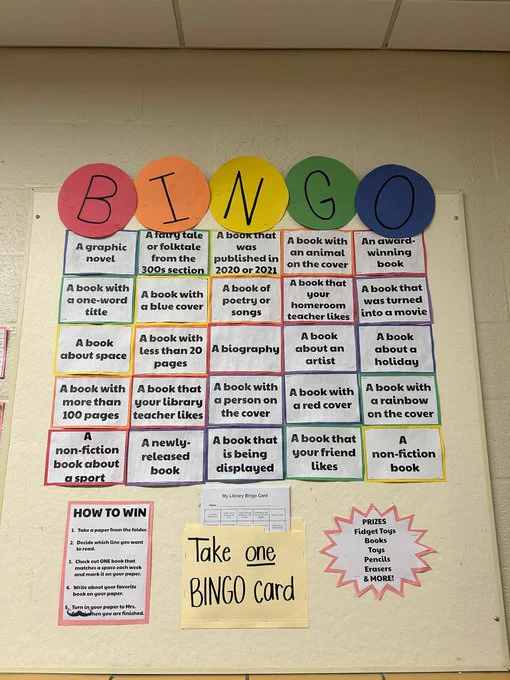 Bulletin board display with bingo ball-like circles of paper at the top spelling out "BINGO." Beneath is a bingo board with criteria like "A graphic novel," "A book with a blue cover," etc.