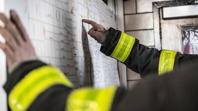 Firefighters in black and yellow uniforms look at a map.