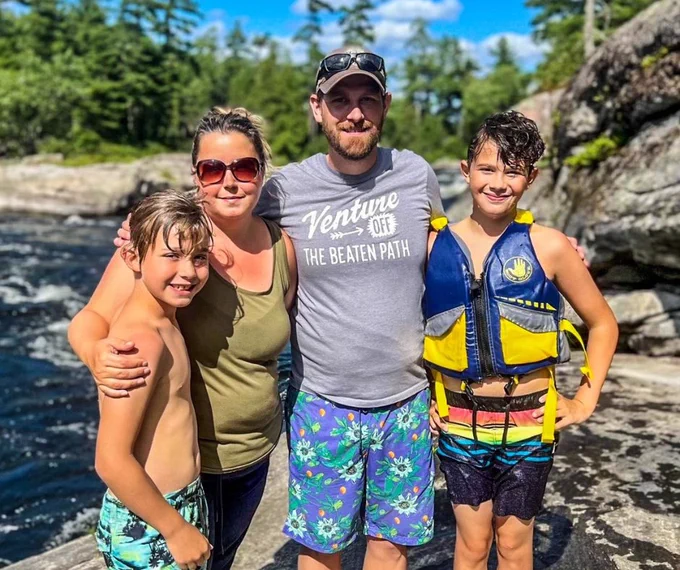 Tyler smiling outdoors with his wife and 2 sons.