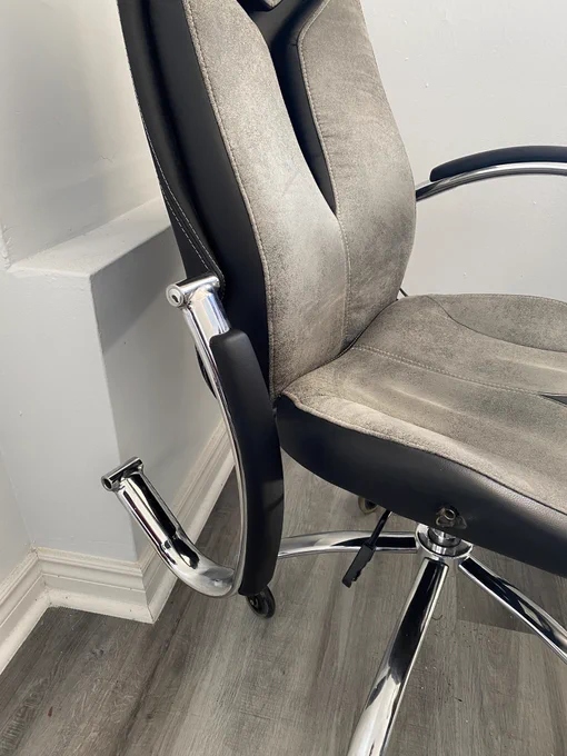 Photo of a grey and black office chair. The right arm of the chair is hanging off, after having disconnected from the lower support bolt.