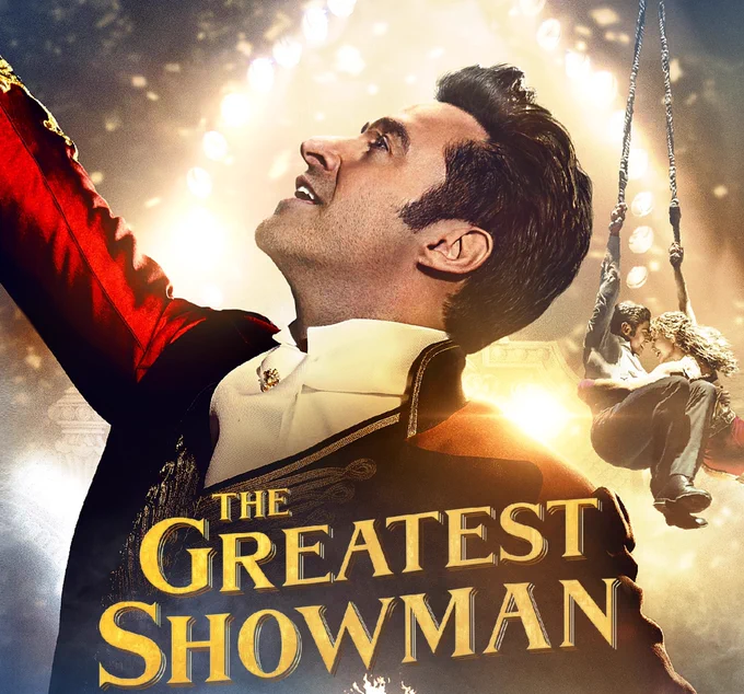 Hugh Jackman dresses as a ringmaster and the words the greatest showman, in the background two people swing on ropes