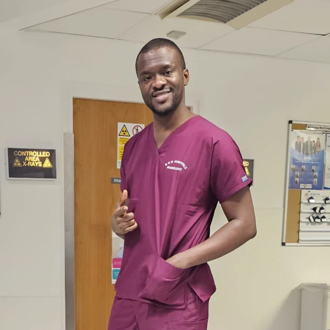 Photo of Baba standing on a ward in his uniform, smiling and giving a thumbs up to the camera.