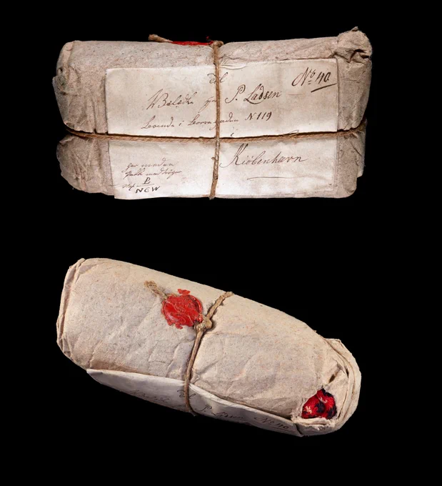 Two still-sealed packages (but you can see a glimpse of red coloured wool in one corner), black background.
Credits: Prize Papers Project, National Archives, ref. HCA 32/952, Images reproduced by permission of The National Archives, UK, Photographer: Maria Cardamone.