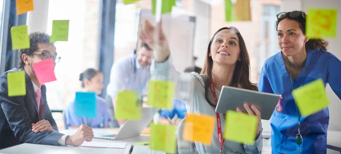 A woman pointing to a wall of post-it notes.