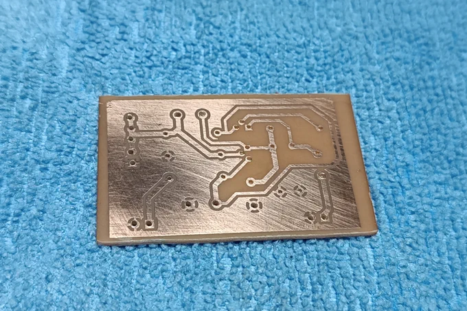 The bottom side of the small PCB once etched, resting over a light blue towel