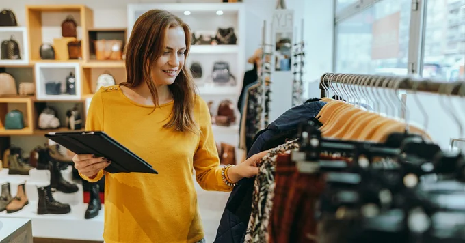 Women with a clipboard looking at clothes in a retail shop. 
