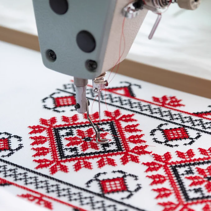 A close-up view of the needle of a digital embroidery machine and a folksy black and red embroidery project.