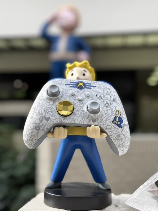 A Vault Boy figurine holding up the Vault Dweller version of the Fallout Edition Xbox Wireless Controllers from Xbox Design Labs.