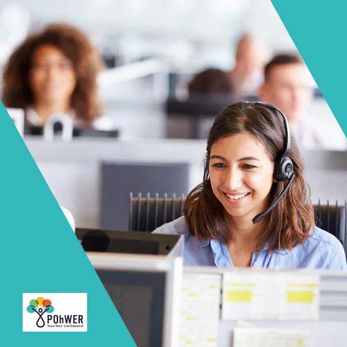 A young woman is sat at a desk in a call centre wearing a headset and smiling
