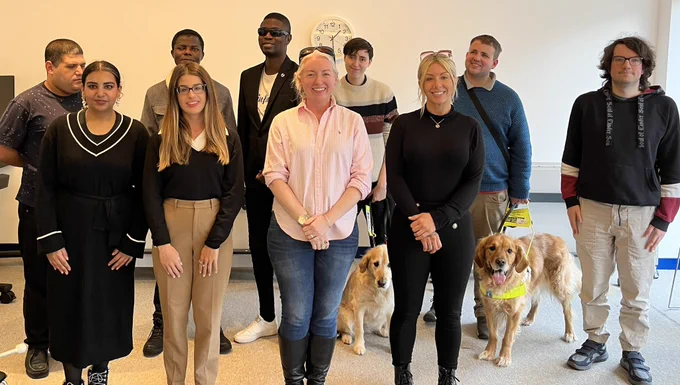 Photo shows ten interns and two guide dogs standing in front of a wall all smiling and looking happy