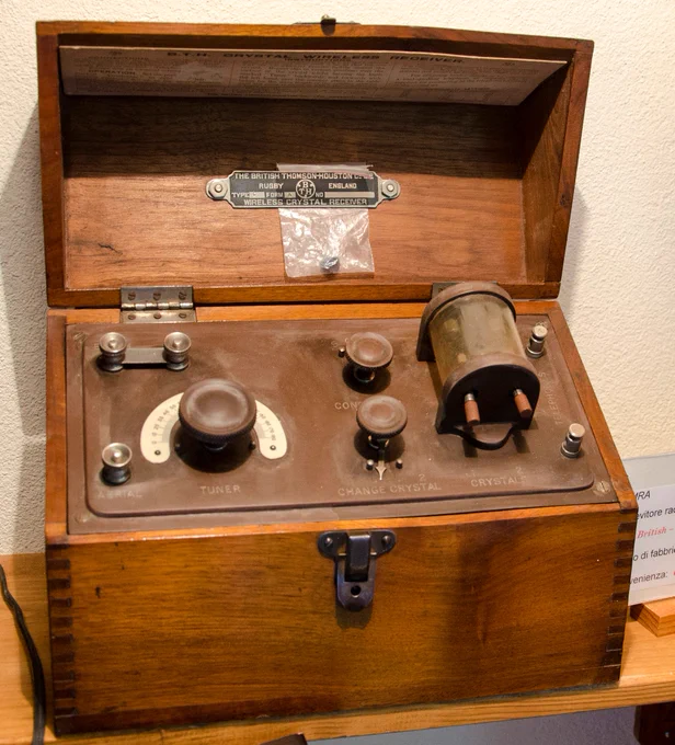 A crystal radio set with wooden casing on display at the Museo della Radio in Switzerland. The set’s lid is open. The radio set was made by British Thomson-Houston and manufactured c.1915. 