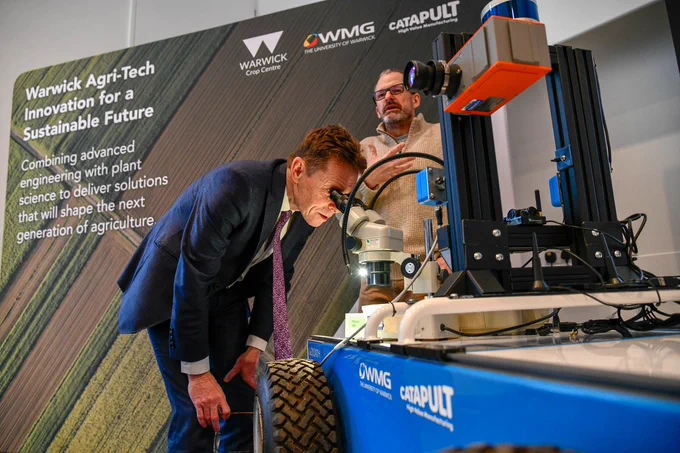 Andy Street looks into a microscope, in front of a WMG Afri-Tech sign.