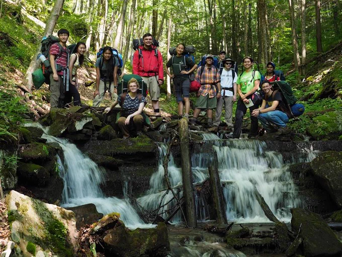 Students standing at the top of a waterfall in the woods at the National Youth Science Camp