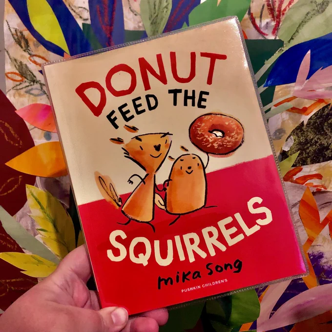 Graphic novel "Donut feed the squirrels" by Mika Song held in front of a colourful collage 