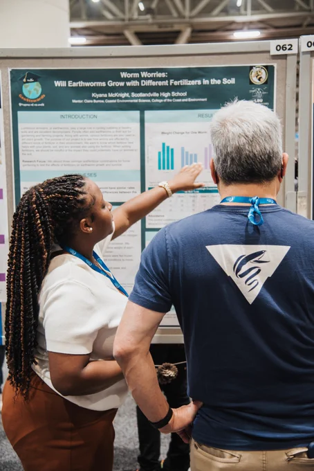 a student explains her research to an attendee at a conference poster session